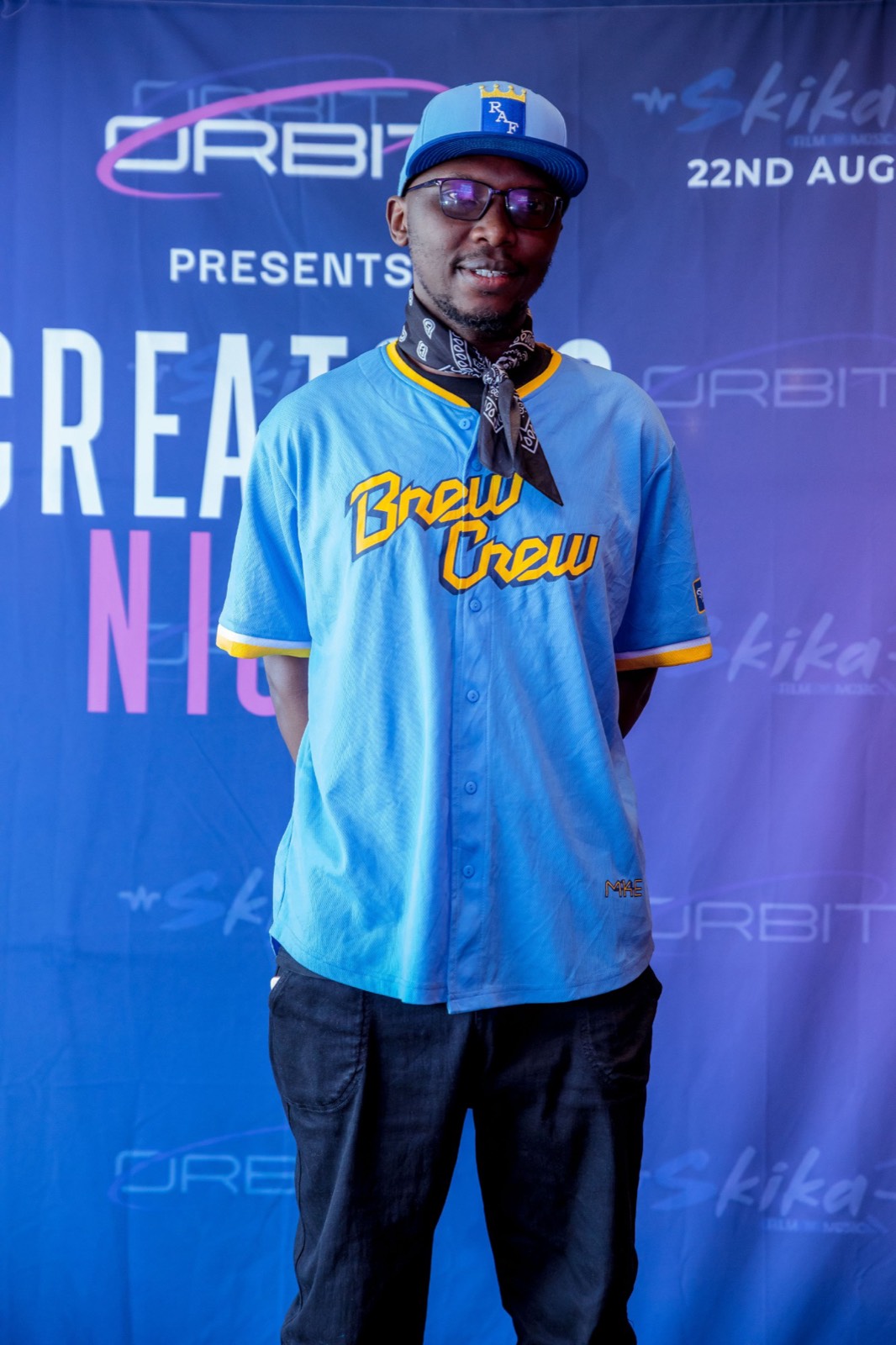 A guest in a light blue baseball jersey and cap at the Creators Night backdrop