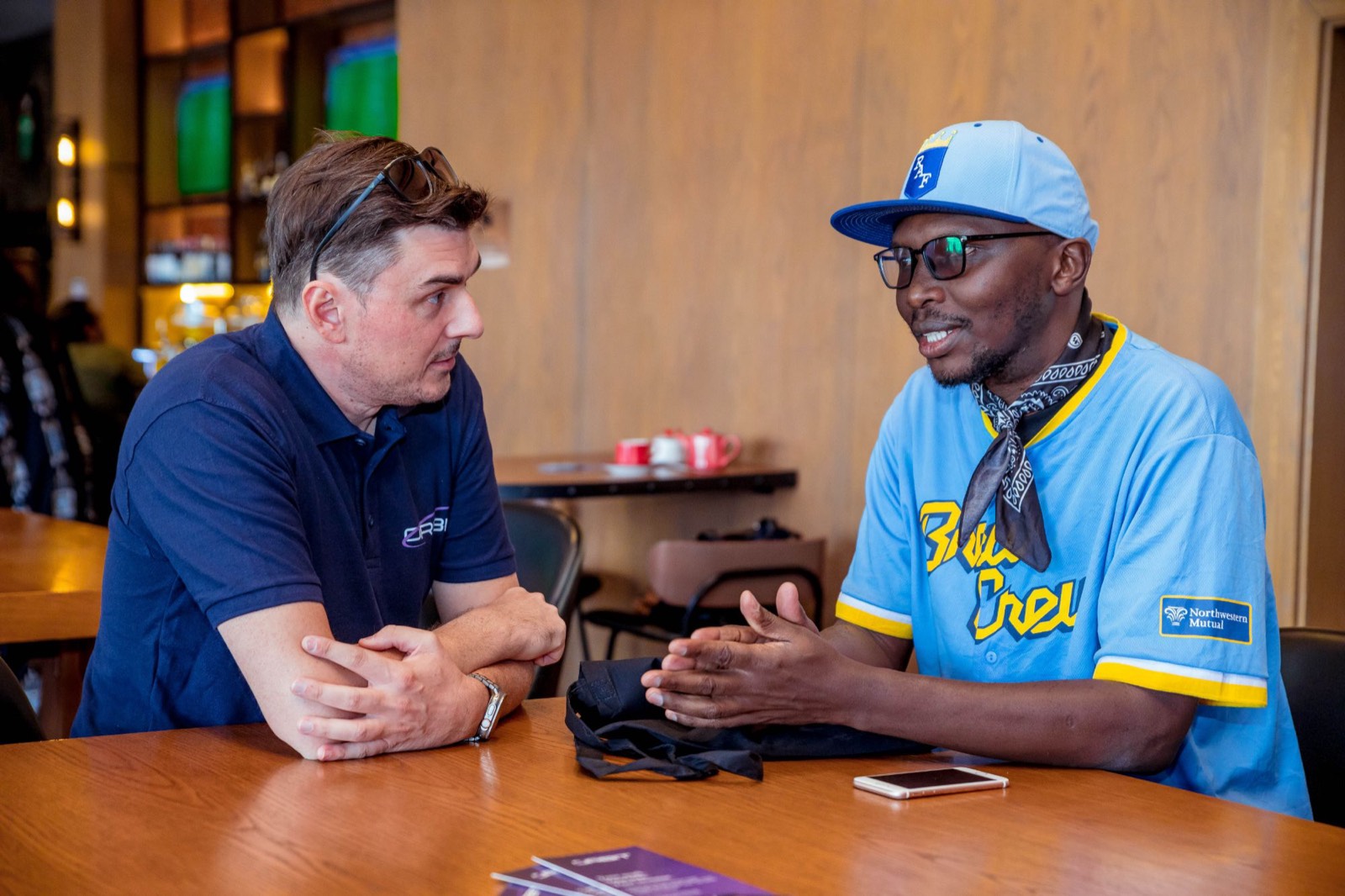 Two people talking across a table, one in an Orbit polo, one in a baseball jersey