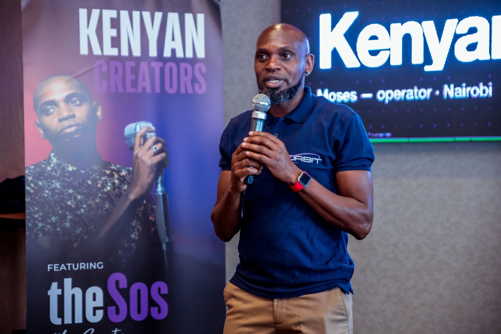 Moses Sospeter speaking into a microphone beside the Kenyan Creators banner